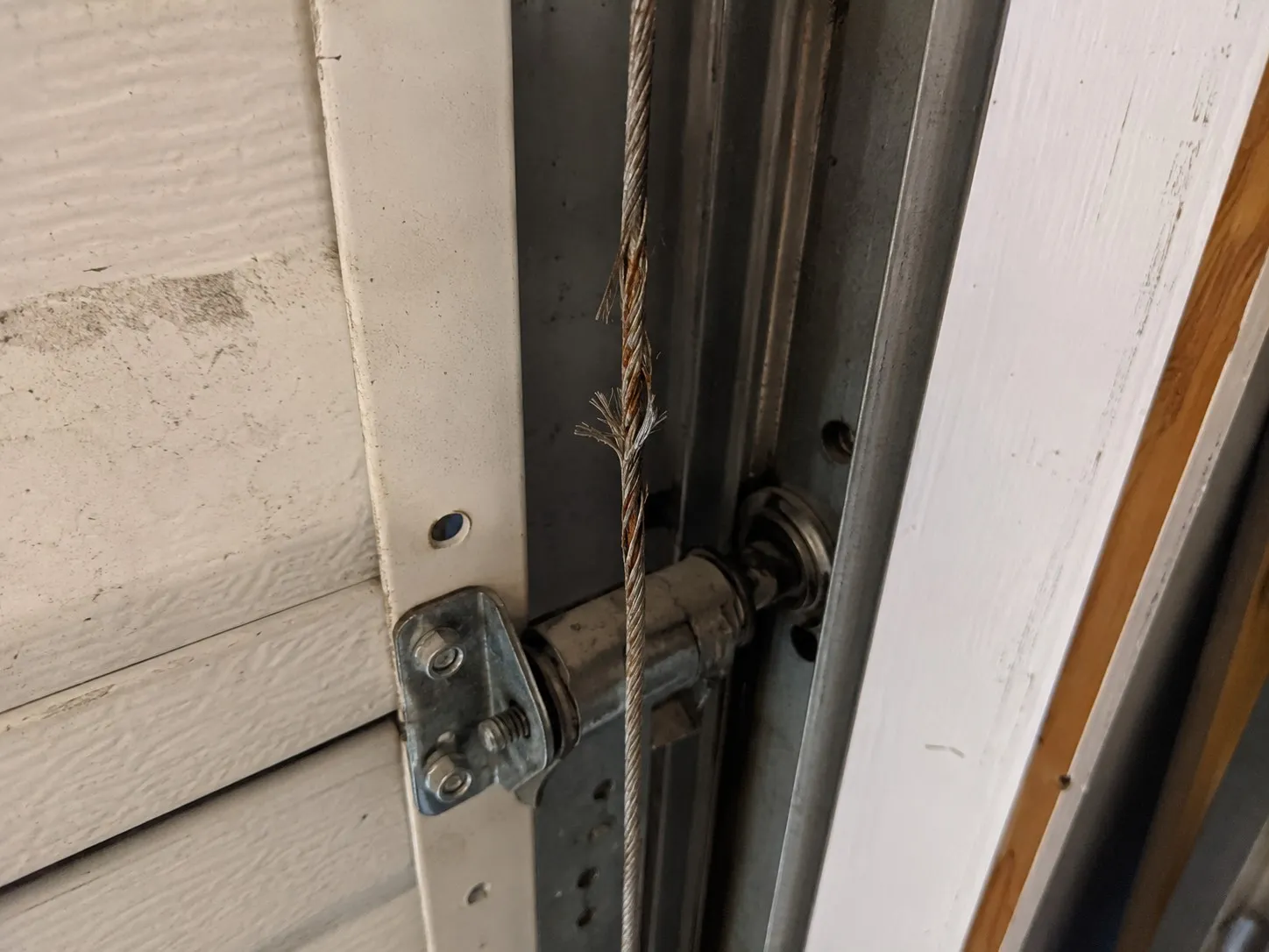 Frayed garage door lift cable with broken strands.