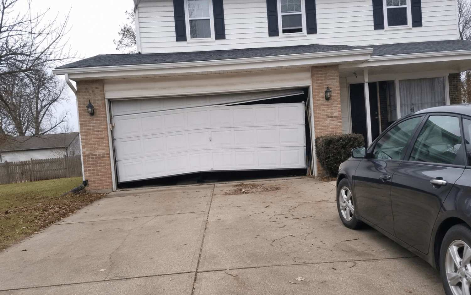 A garage door sagging off its track, with the top corner pulled inward and rollers out of the rail.