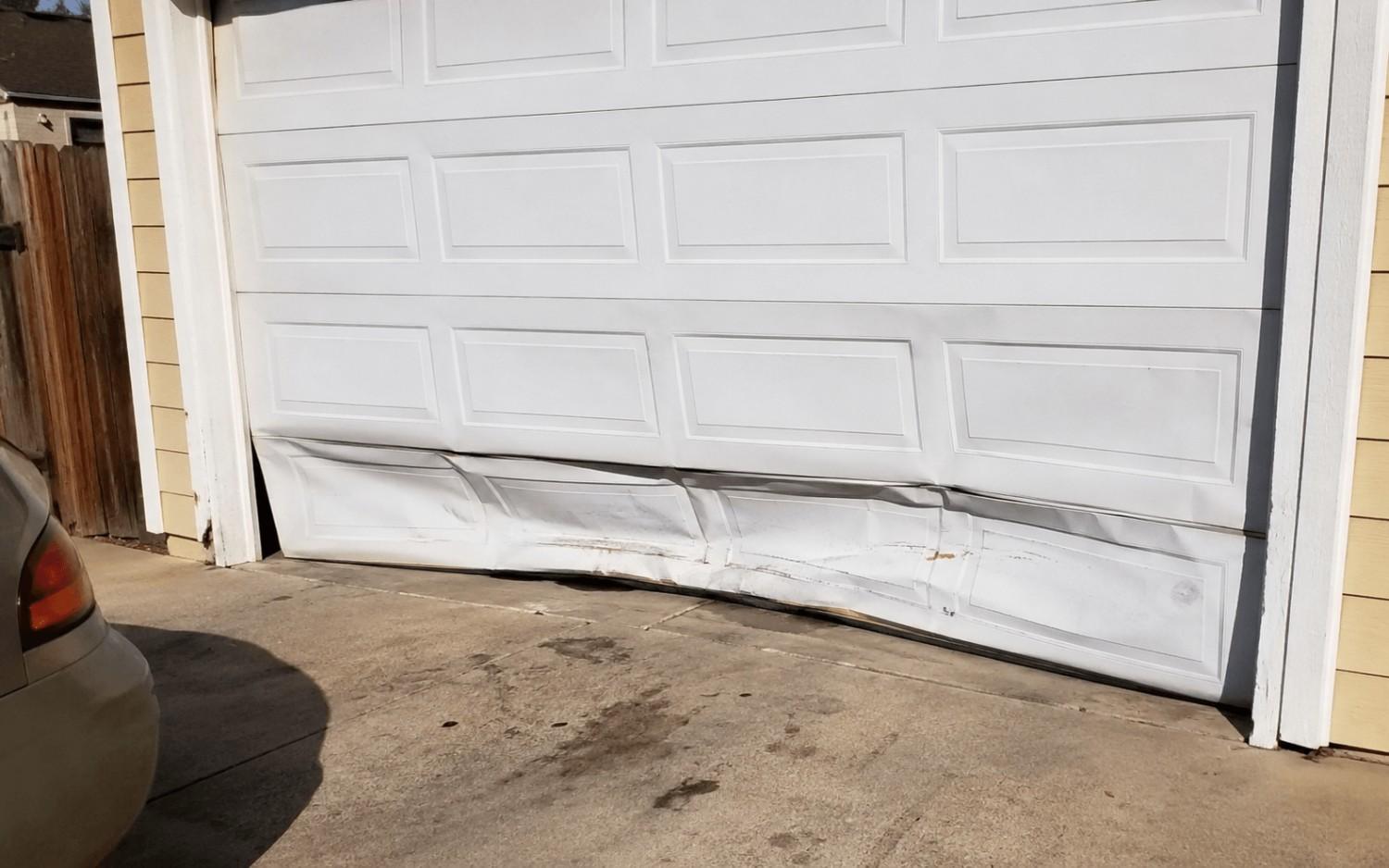 A garage door with its bottom panels caved in and creased after a vehicle backed into it.