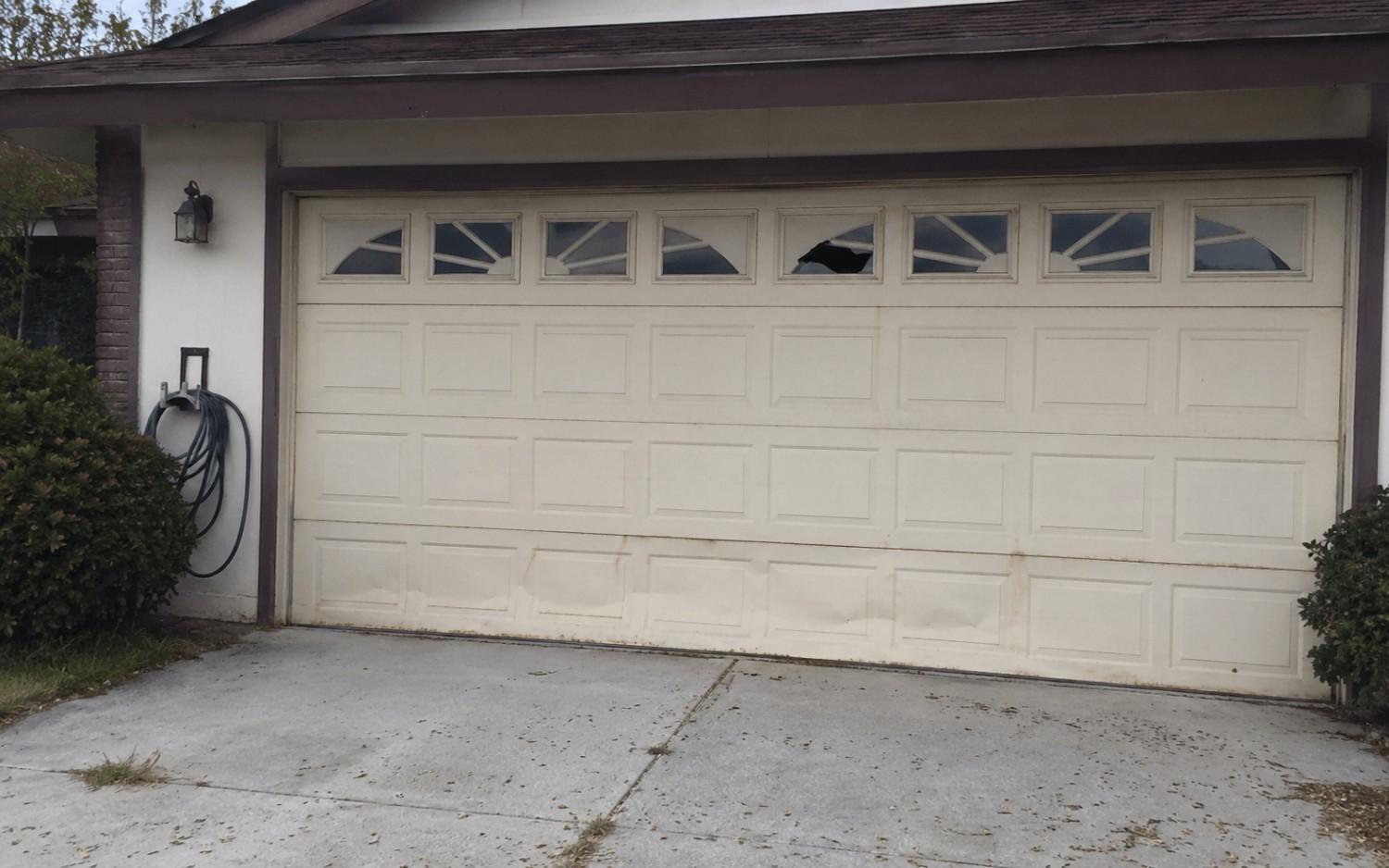 A dated garage door with faded paint, dents along the bottom, and rust bleeding at the seams.