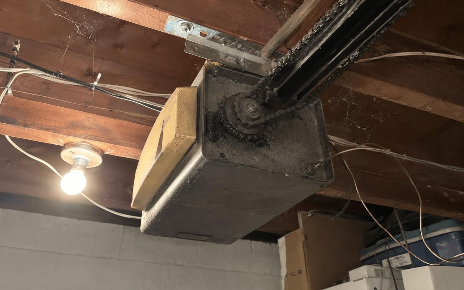 An old chain-drive opener on the garage ceiling with worn parts and loose, tangled wiring.