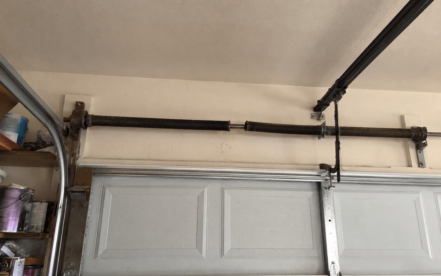 Snapped torsion spring above a closed garage door, with a clear gap where the coil broke apart.