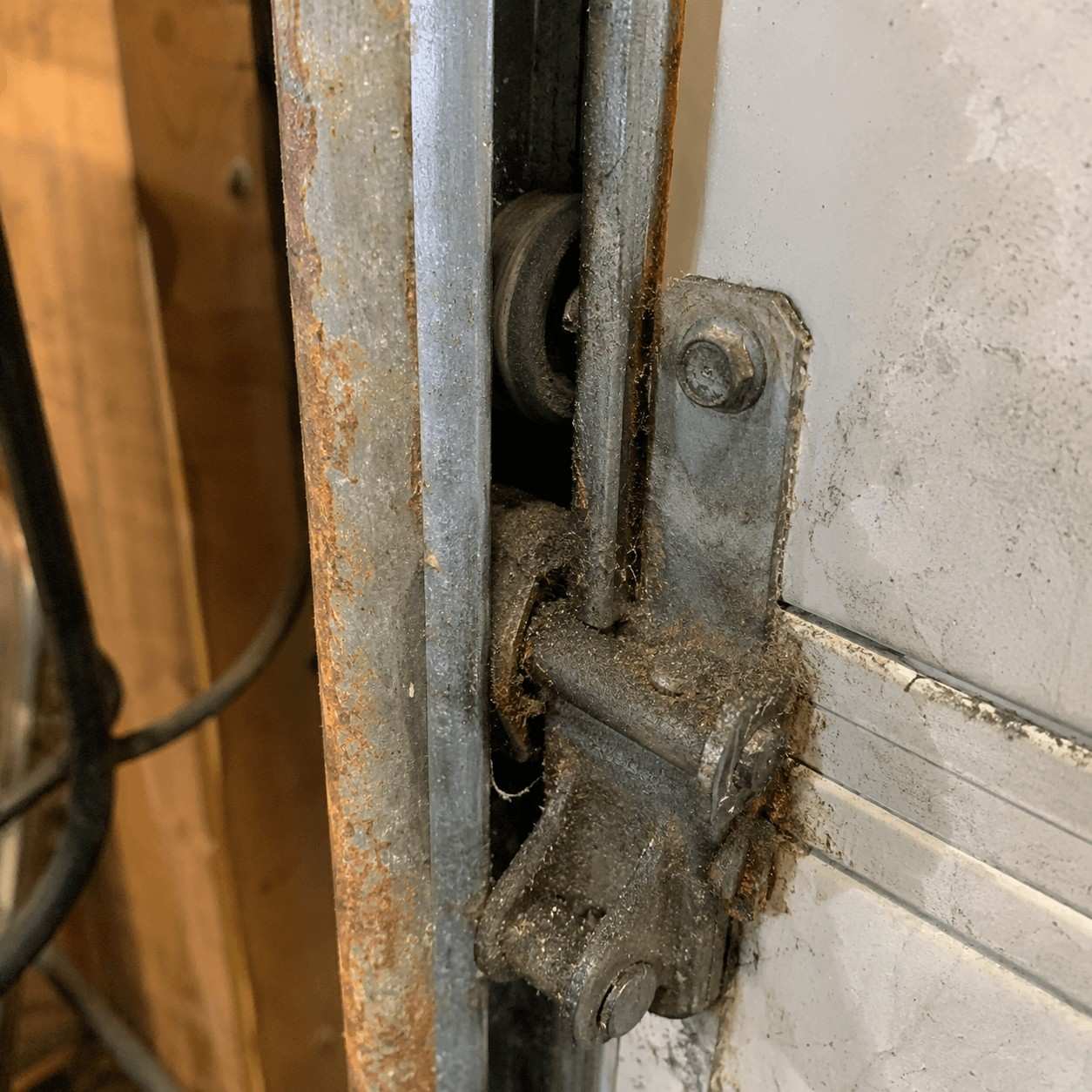 A garage door track and hinge gone rusty and dry, with grit and old grease crusted in the joints.