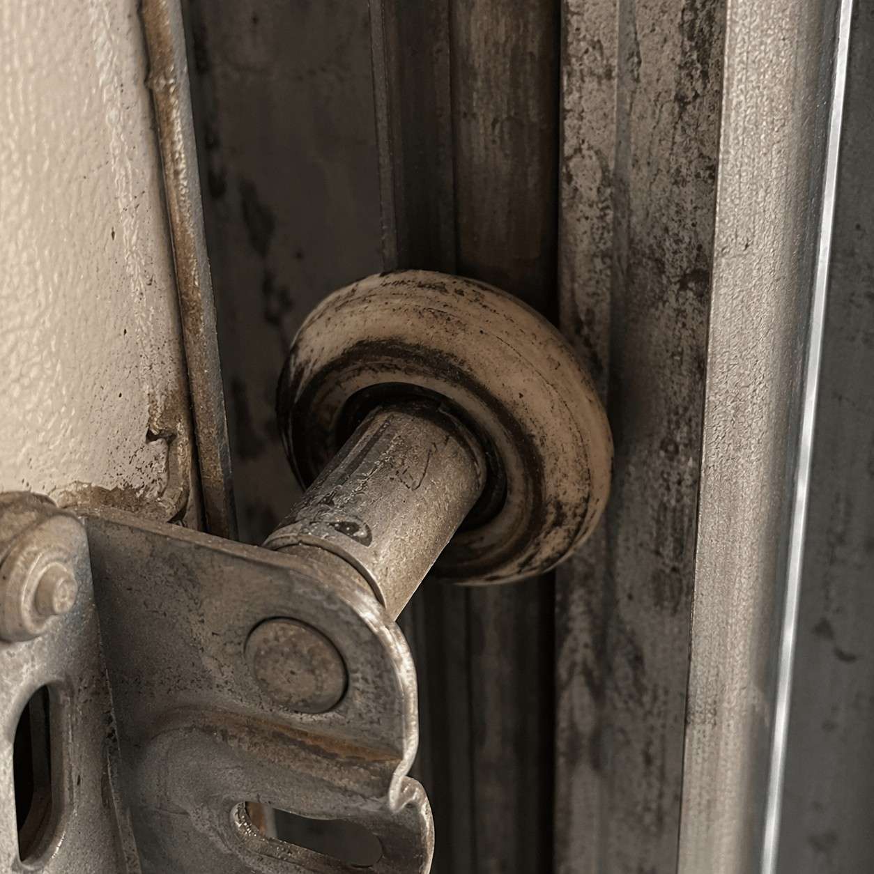 A worn, flat-spotted nylon roller riding in a grimy garage door track.