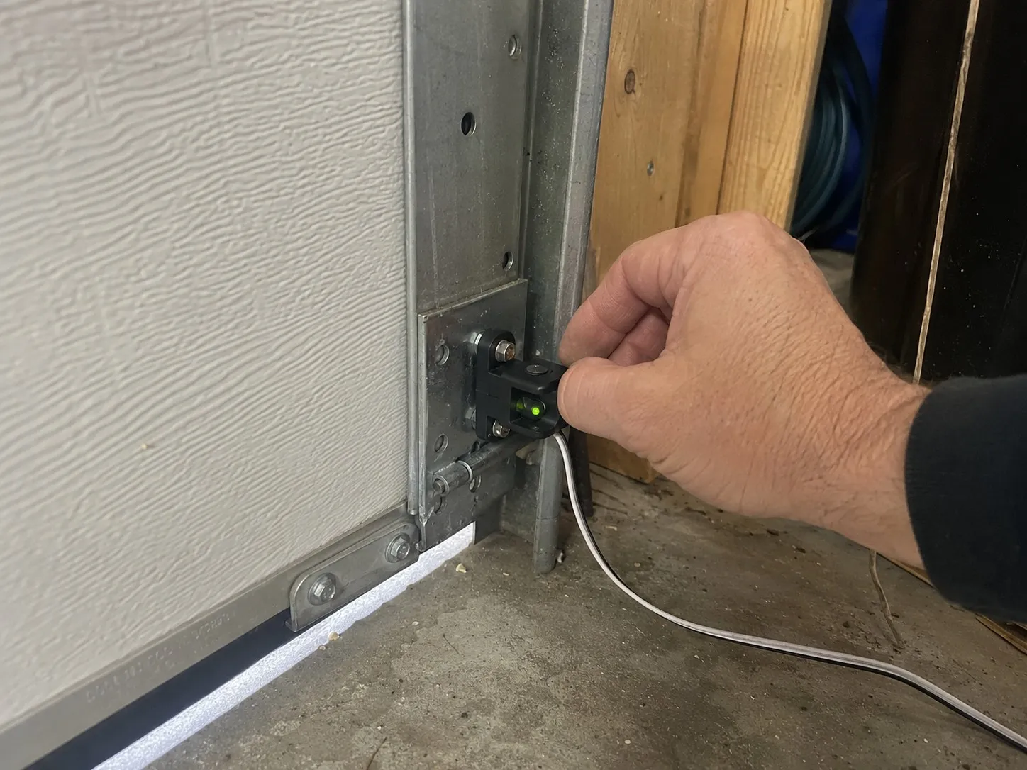 Photo eye safety sensor mounted near the floor of a garage door.