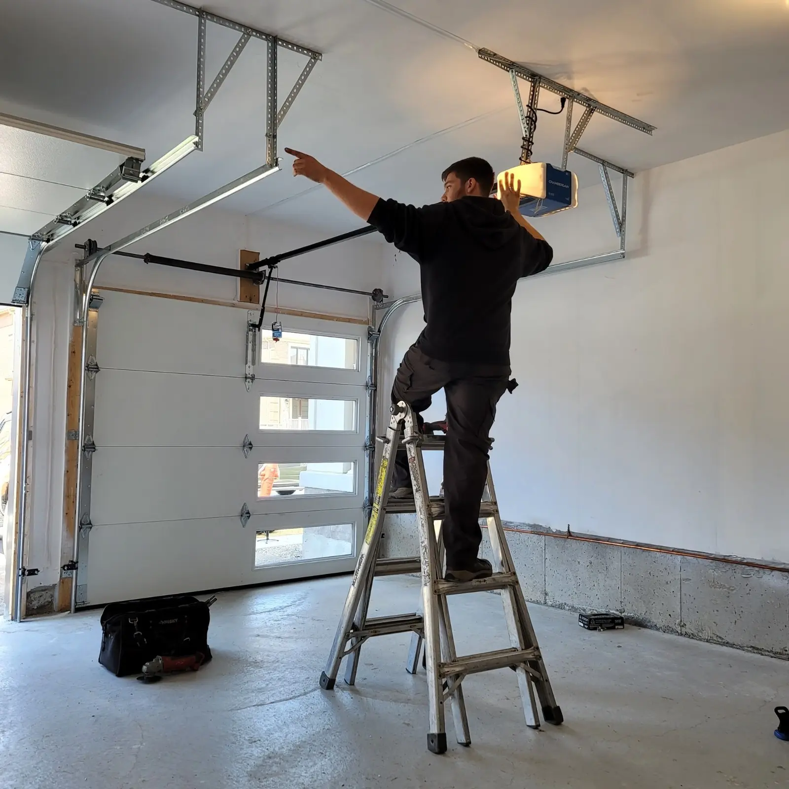 Technician on a ladder installing a garage door opener.